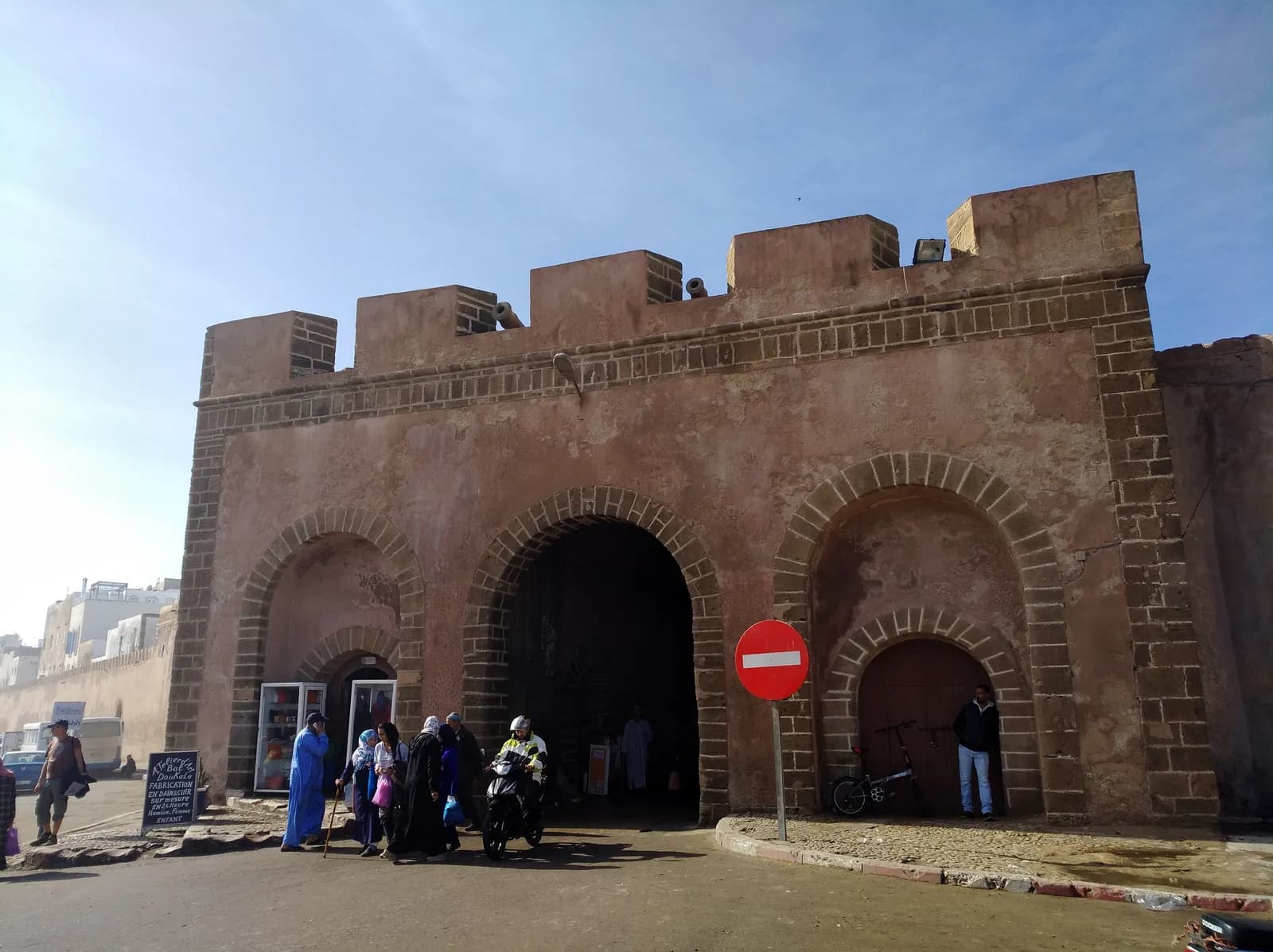 La façade crénelée de Bab Doukkala, trois arches en pierre de taille, canons sur le sommet et passants devant la porte