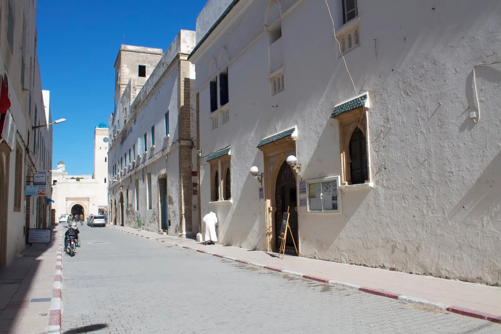 Façade blanche de Dar Souiri, auvents de tuiles vertes et porte en bois, sur une rue pavée de la médina
