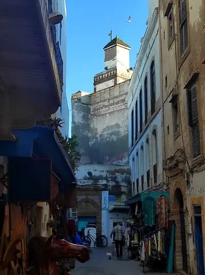 A white-and-blue medina street in Essaouira leading to a fortified tower