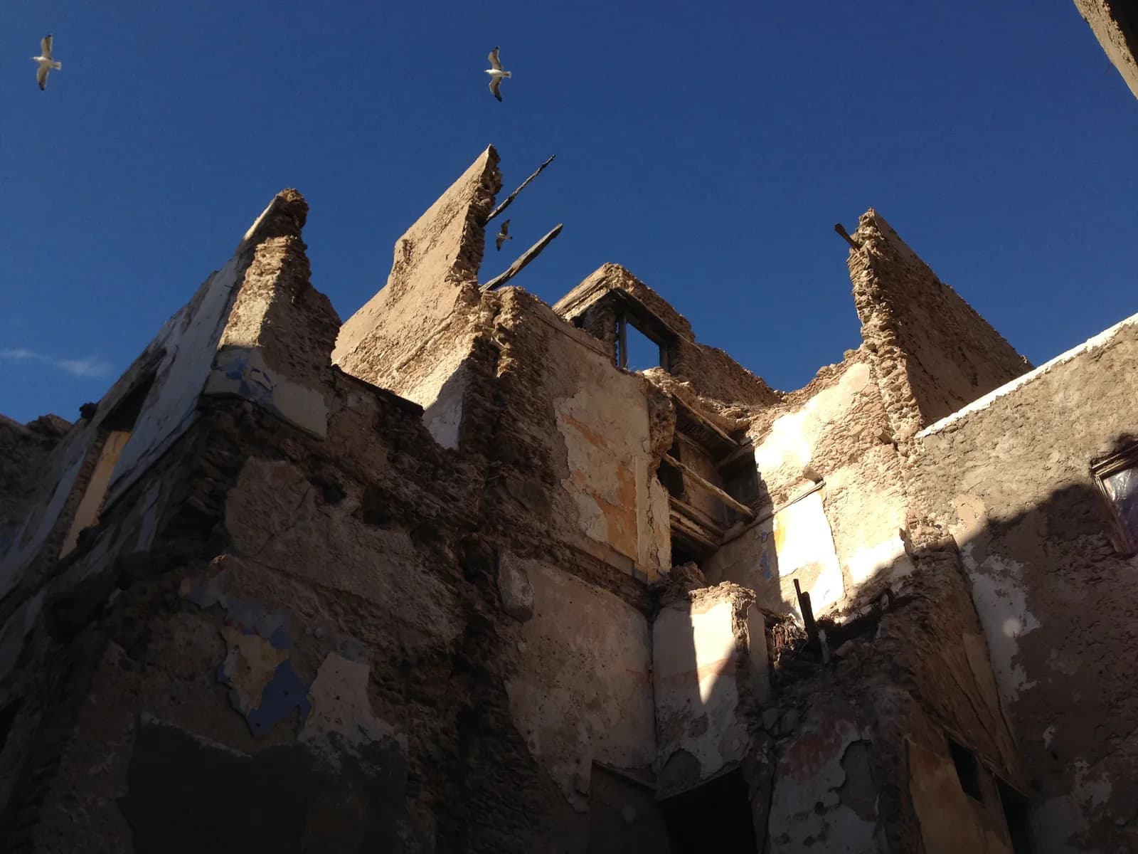 Murs éventrés d’une maison en ruine du Mellah d’Essaouira, pierre et enduits écaillés sous un ciel bleu, en 2014