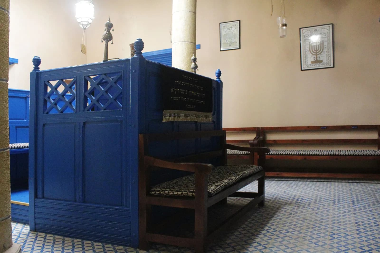 Tébah peinte en bleu et banc en bois dans la synagogue Haïm Pinto, sol en carreaux bleus et blancs, menorah encadrée au mur