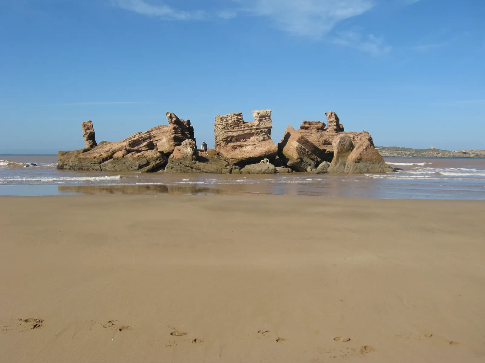 Les ruines du Bordj El Berod sur leurs rochers, entourées d’eau à marée basse, sable mouillé au premier plan