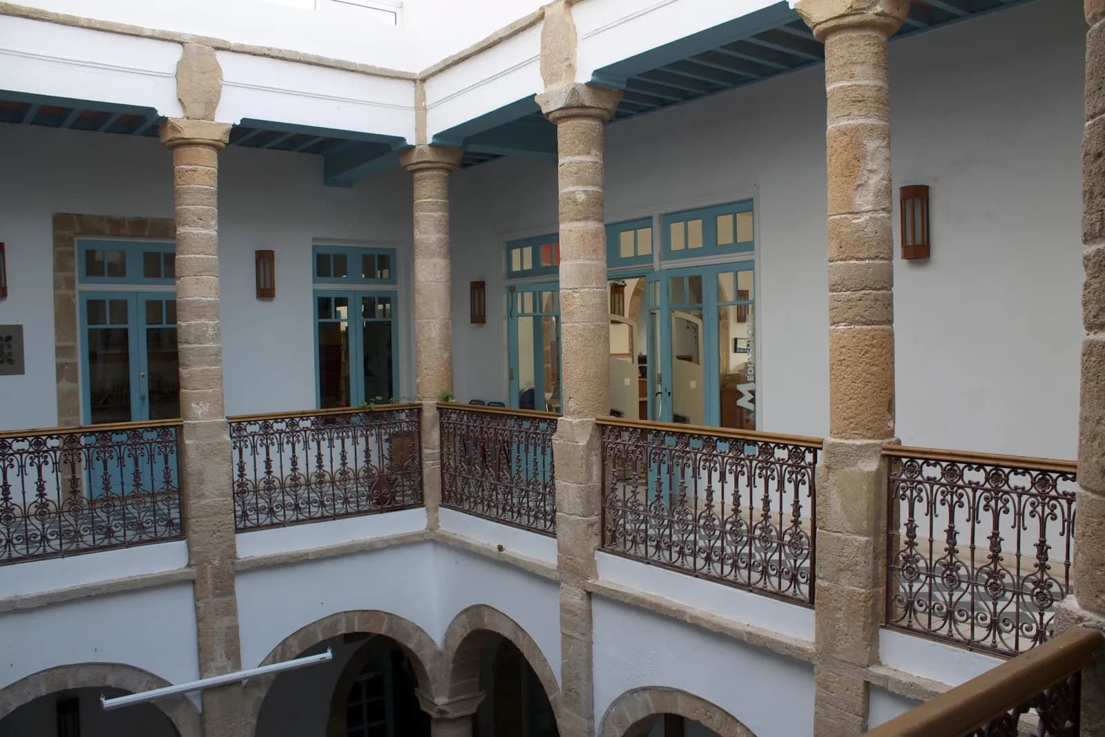 Galerie à l’étage du patio de l’ancien consulat de France, colonnes en pierre, balustrades en fer forgé et portes bleues