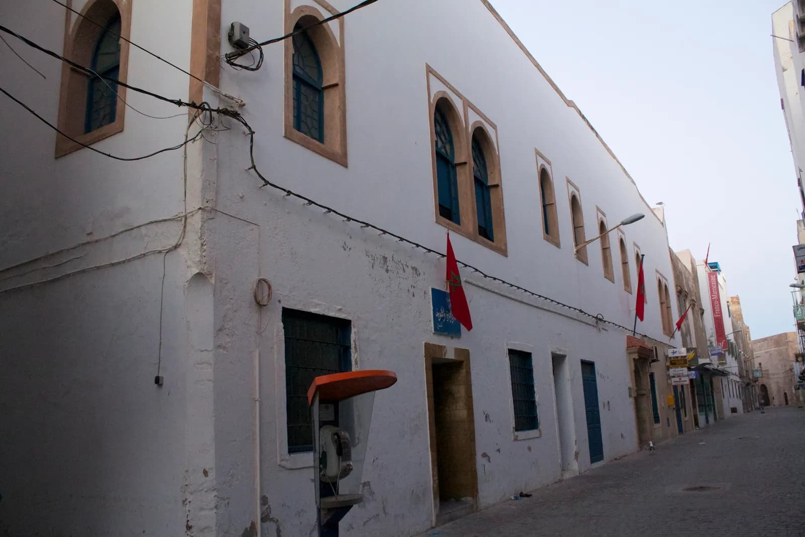 Façade blanche du musée Sidi Mohamed Ben Abdallah, fenêtres en arc et drapeaux marocains, rue de la médina au matin