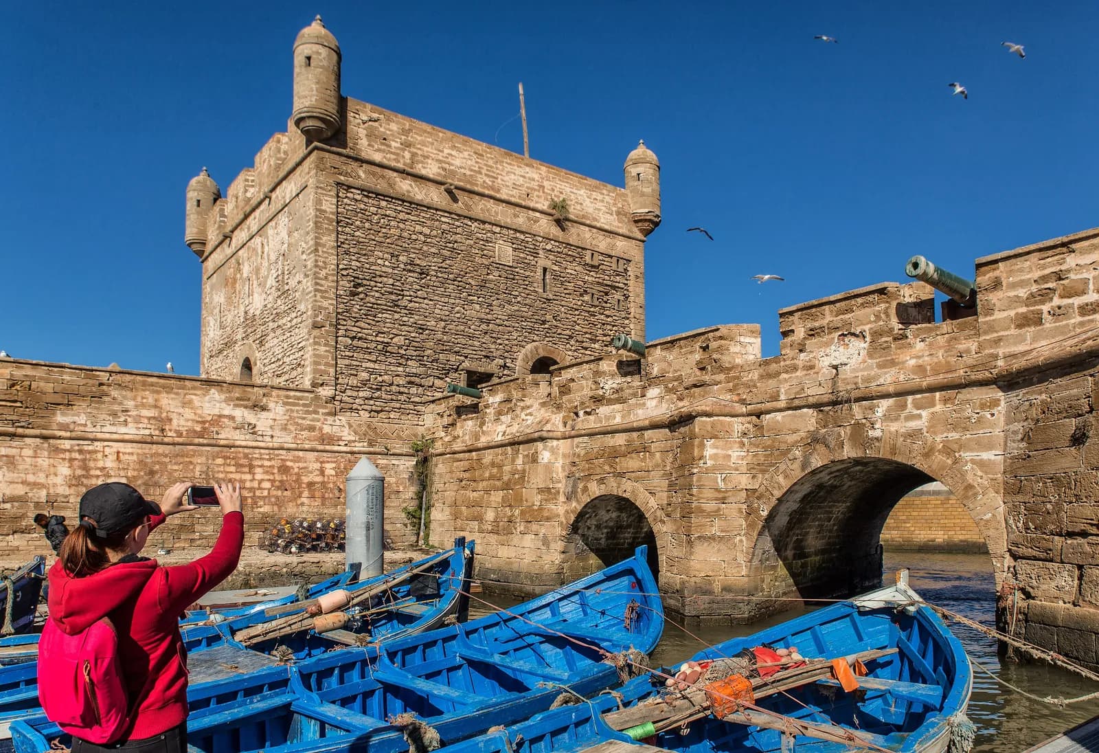 La tour carrée et le pont en arches de la Skala du Port, canons sur le parapet, barques bleues amarrées au pied